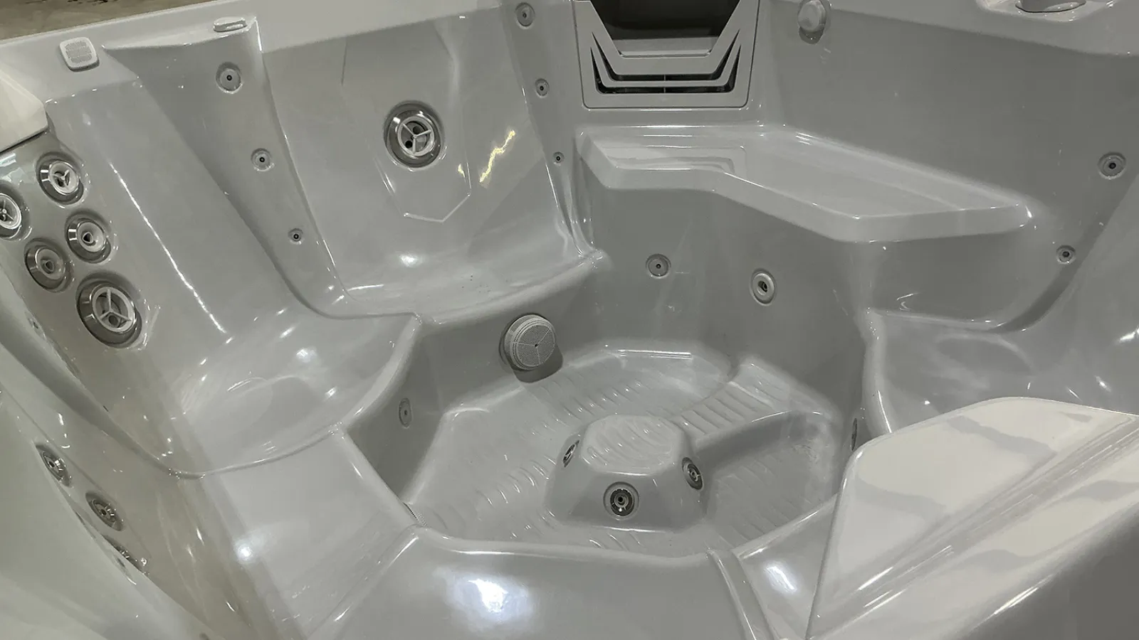 Empty white luxury hot tub with multiple jet nozzles and contoured seating for relaxation.