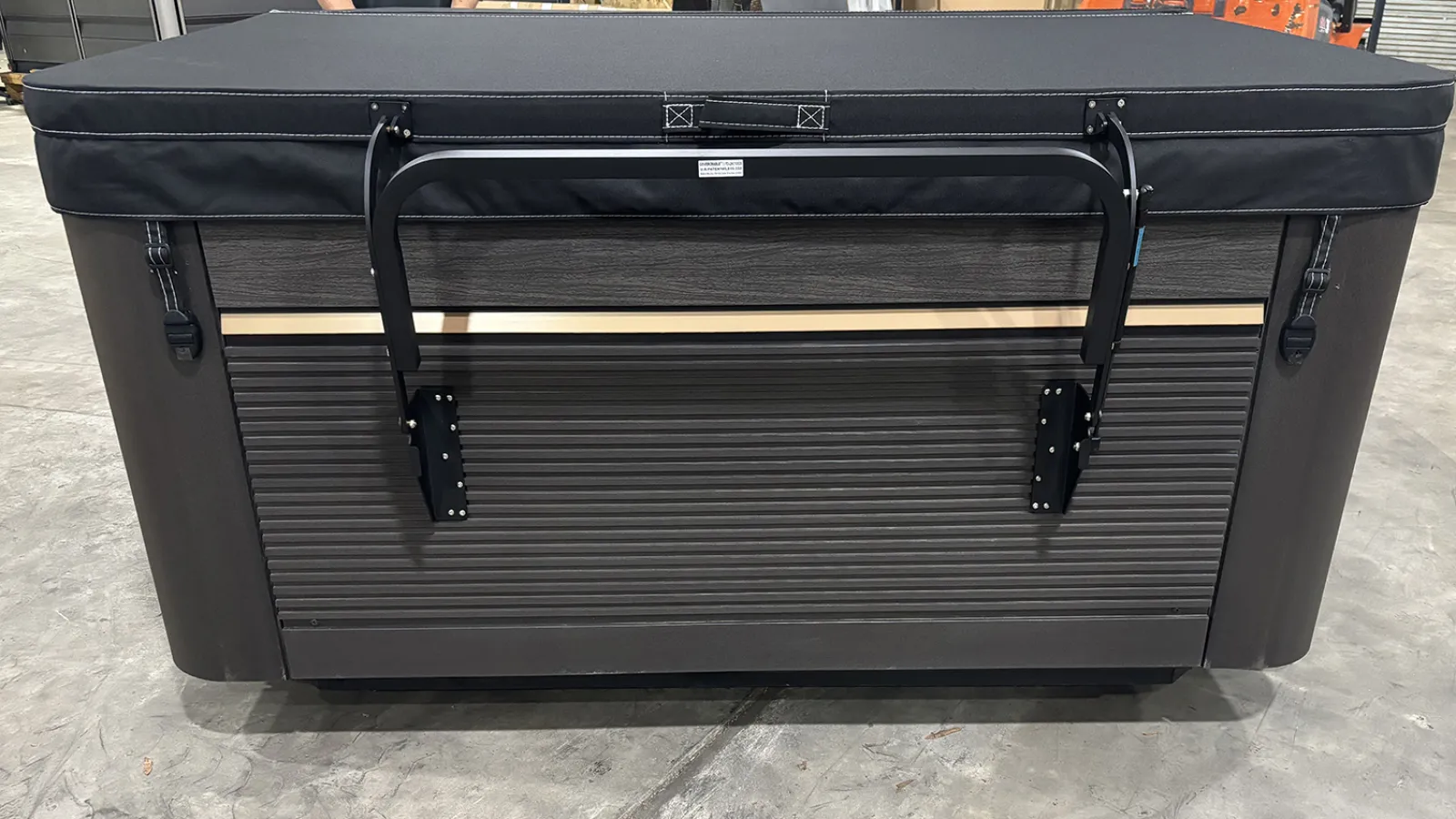 Closed dark brown hot tub with black cover and sturdy lift assist system in indoor warehouse setting.