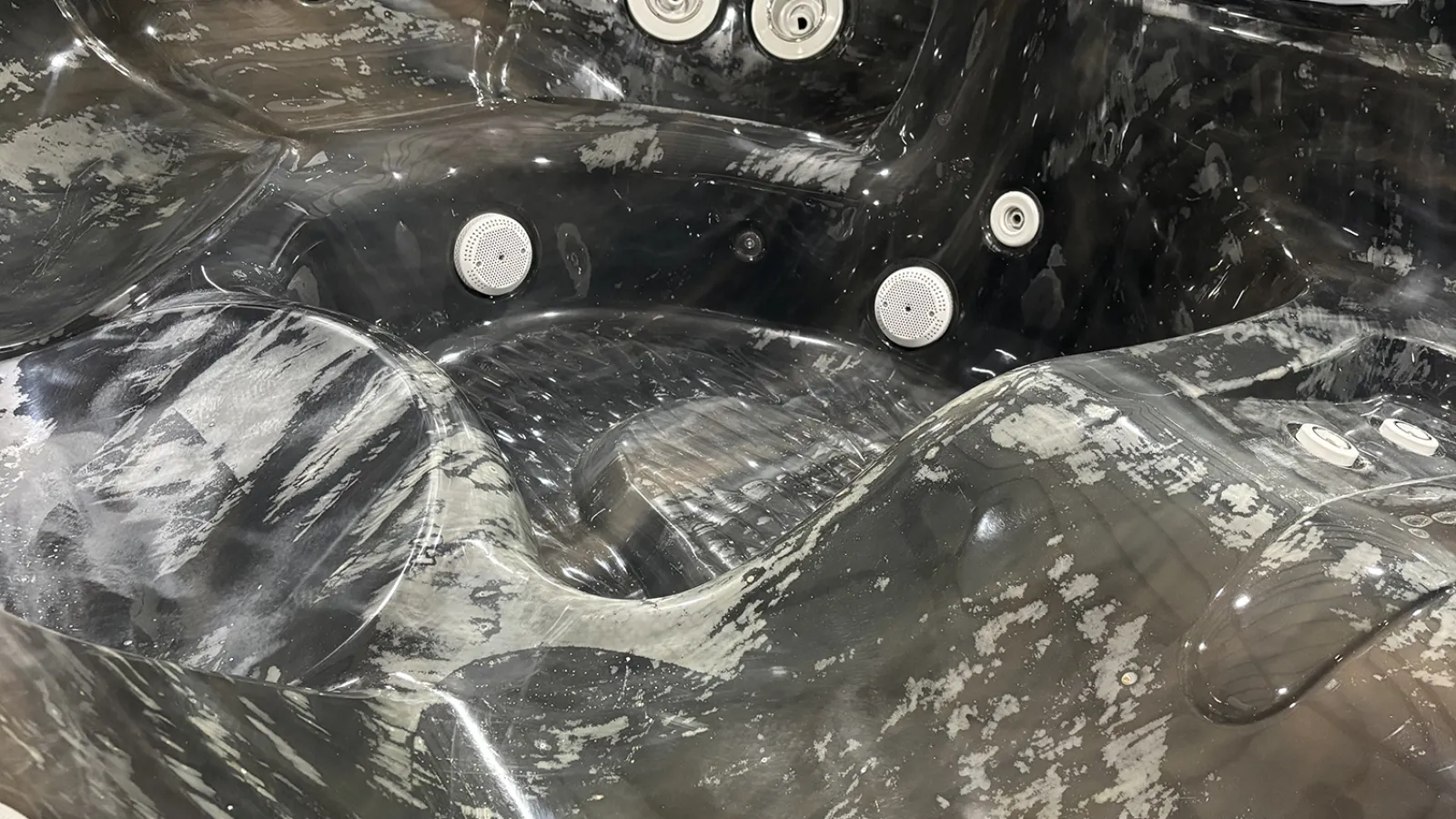 Close-up of an empty black and grey marbled jacuzzi hot tub with multiple jets and ergonomic seats.