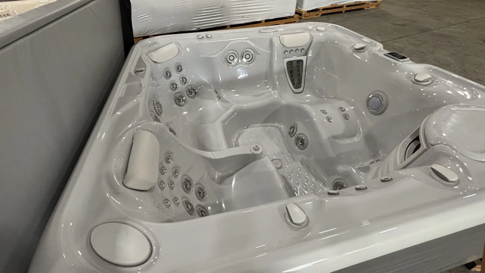 Modern white jacuzzi hot tub with multiple jets and comfortable seating in a warehouse setting