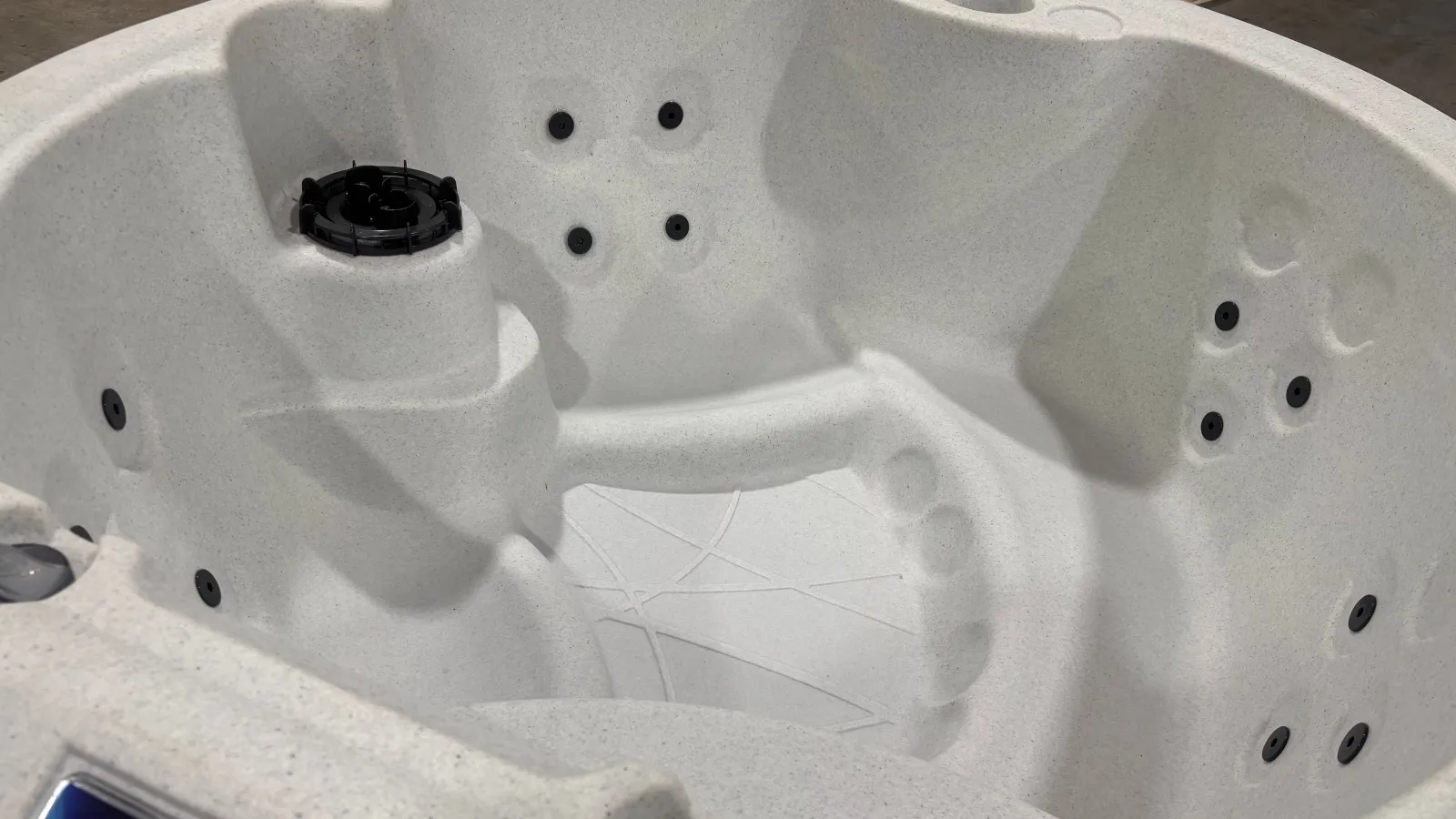 Empty white spa hot tub with multiple black jets and contoured seating in an indoor setting.