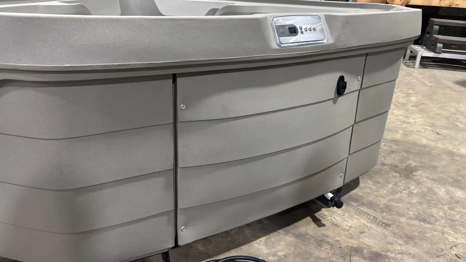 Close-up of a gray outdoor hot tub control panel and exterior paneling on a concrete floor.