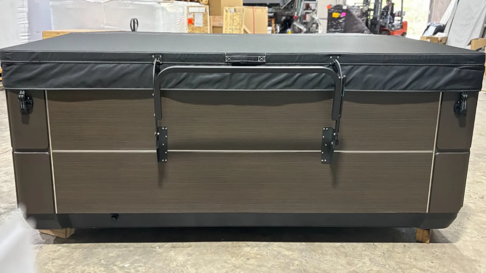 Brown hot tub with black cover secured by metal latch in warehouse setting with industrial surroundings.