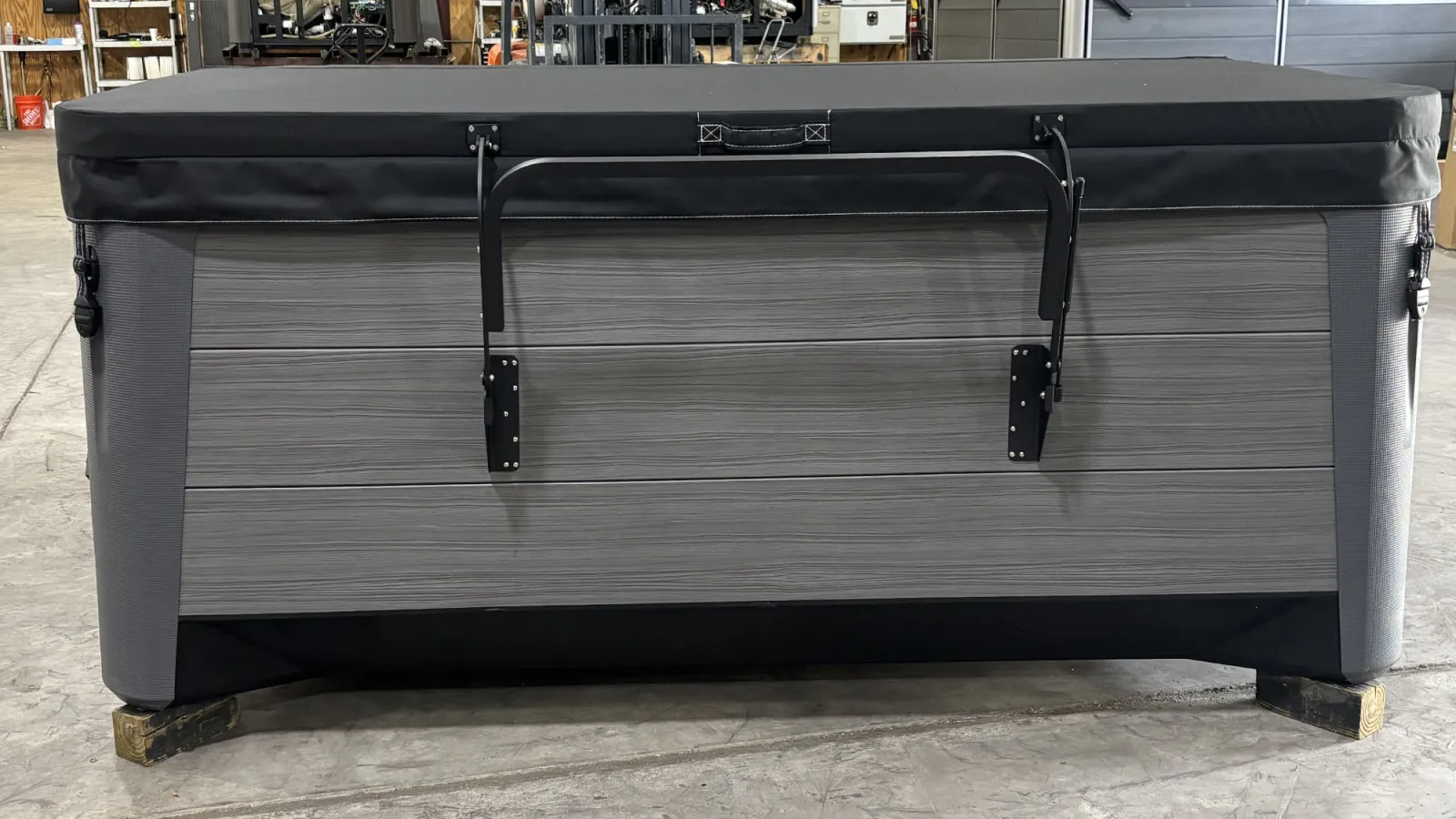 Gray hot tub with black cover and metal handle in an industrial warehouse setting.