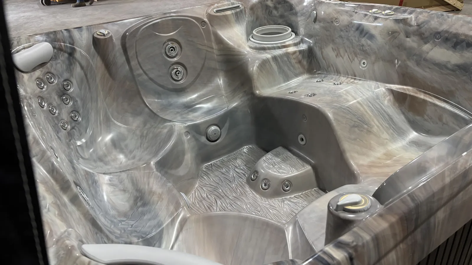 Modern gray marble-patterned hot tub with multiple jets and ergonomic seating in a showroom setting