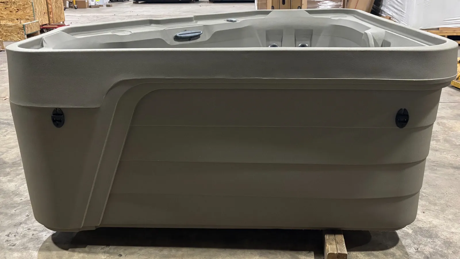 Outdoor hot tub with beige exterior shell placed in warehouse setting on wooden blocks.