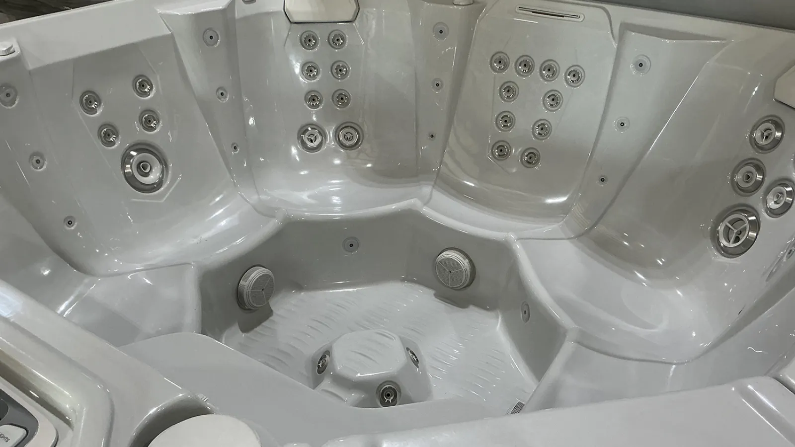 Modern white hot tub with multiple ergonomic seats and numerous water jets for hydrotherapy relaxation.