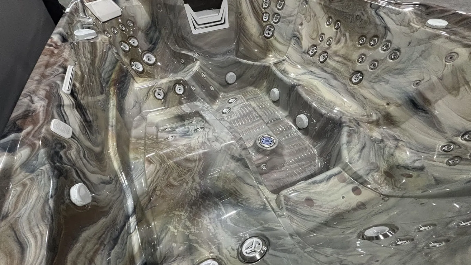 Empty marble-patterned hot tub with multiple jets and ergonomic seating under showroom lighting