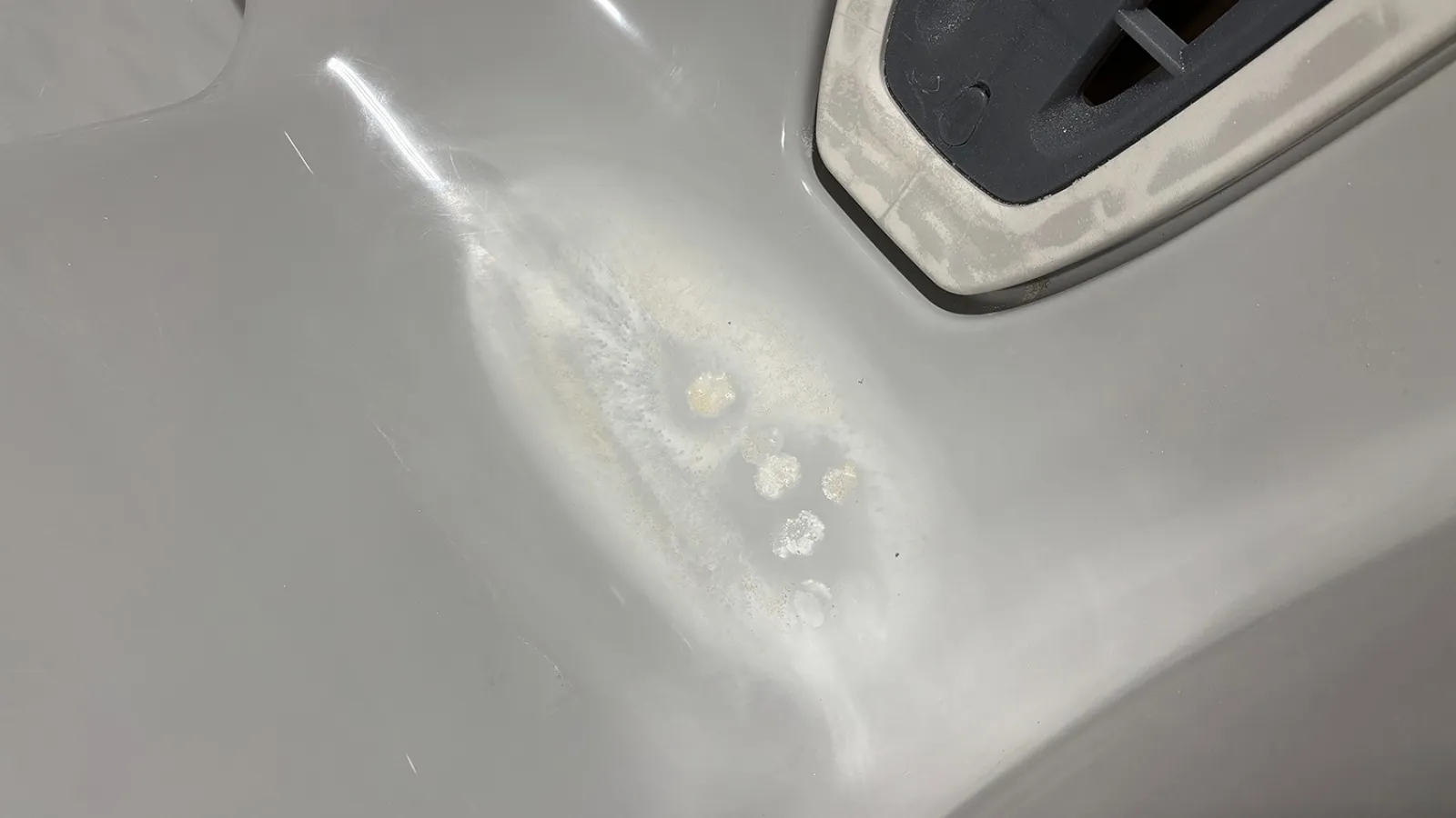 Close-up of a white surface with paint damage and peeling near a black and white object edge.