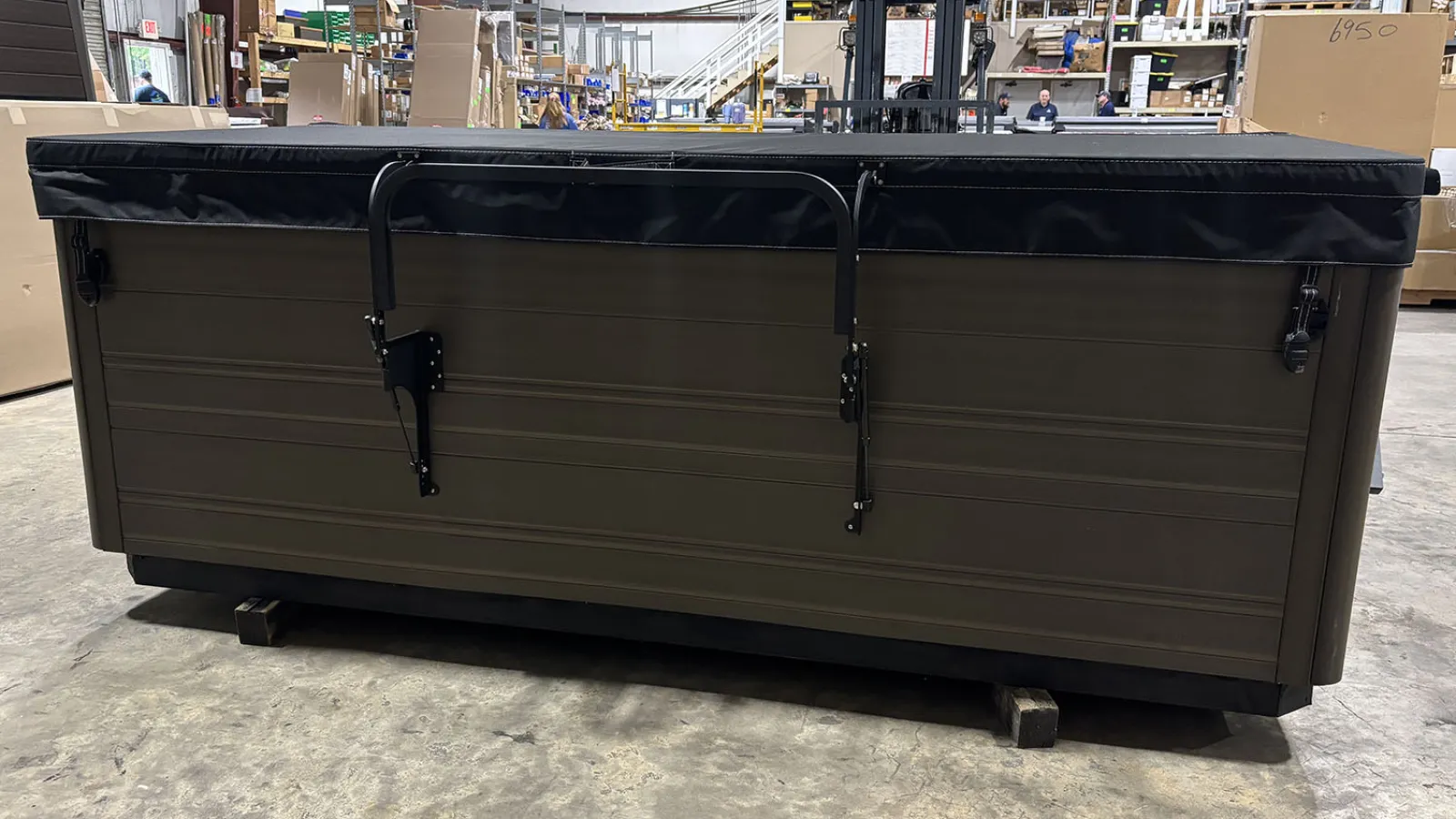 Large rectangular hot tub with a black cover inside a spacious warehouse setting.