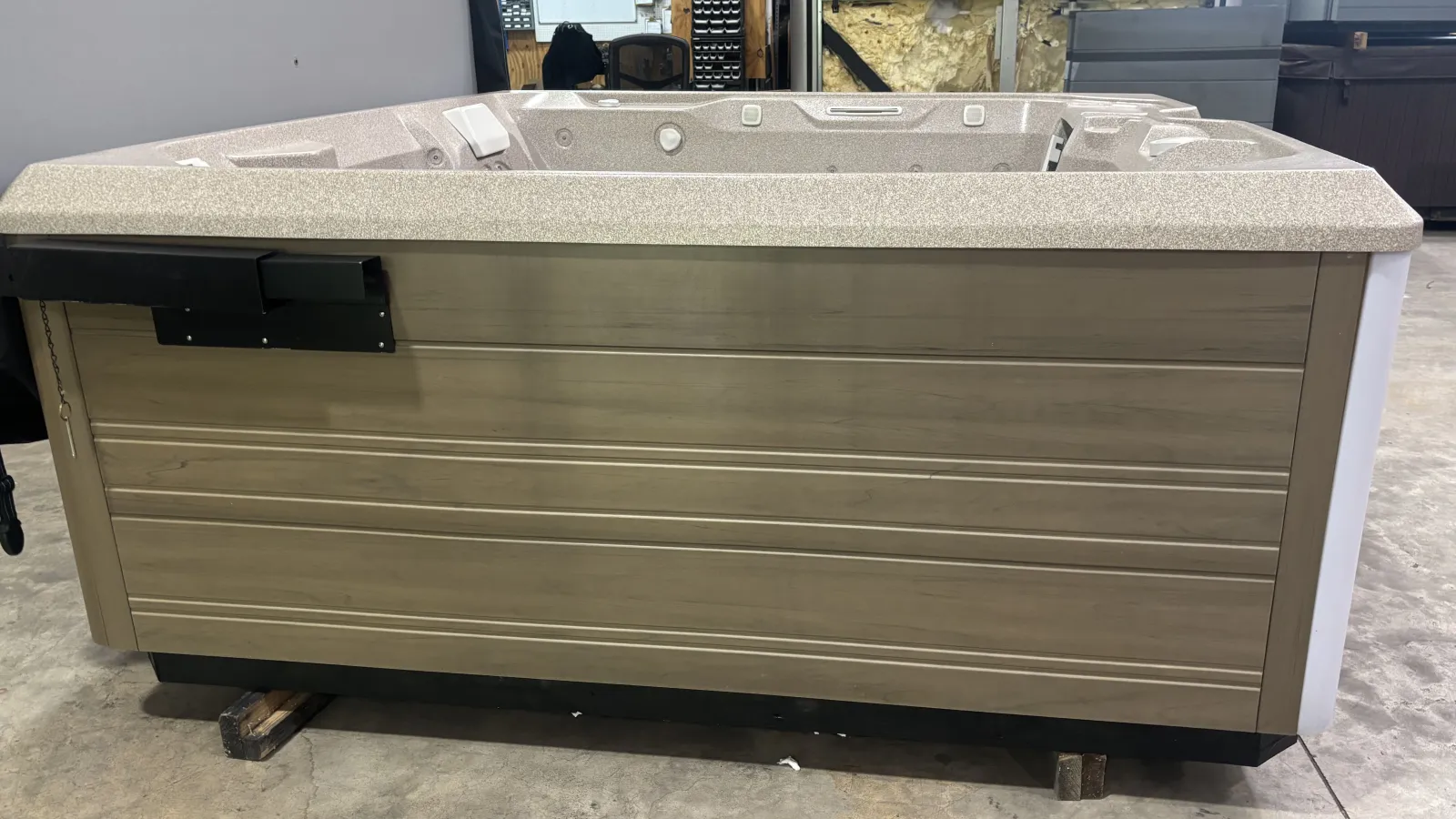 Large beige and tan outdoor hot tub with textured interior and wood panel exterior set on concrete floor.