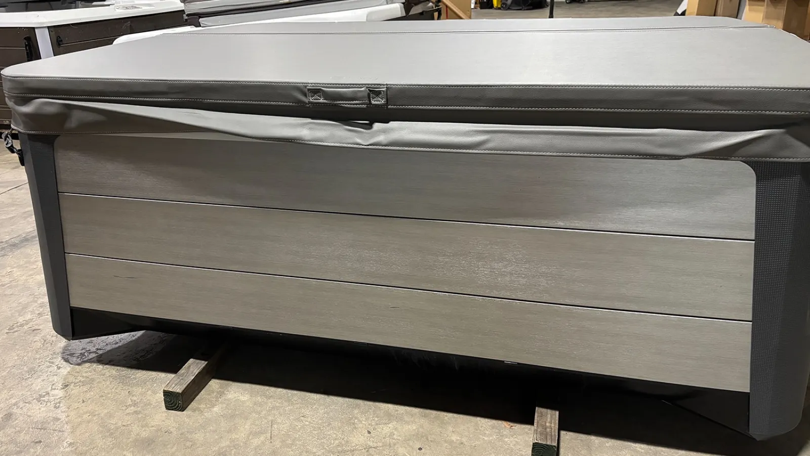 Outdoor hot tub with gray wooden paneling and matching gray cover inside a warehouse.