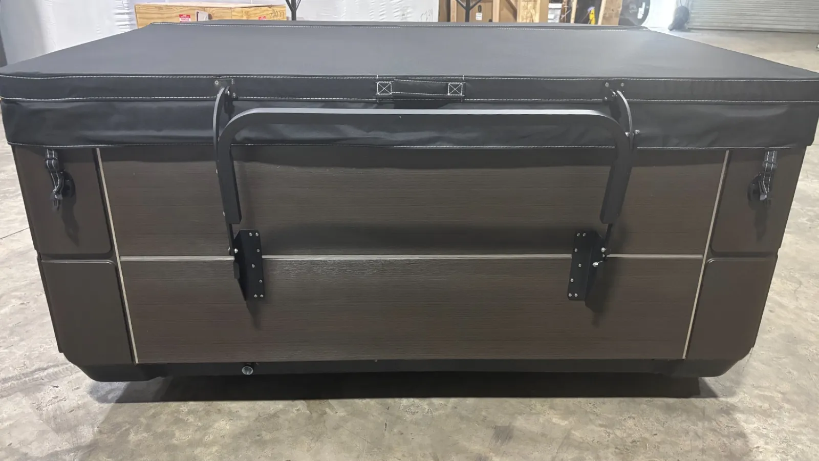 Closed rectangular hot tub with wooden panels and black padded cover in a warehouse setting