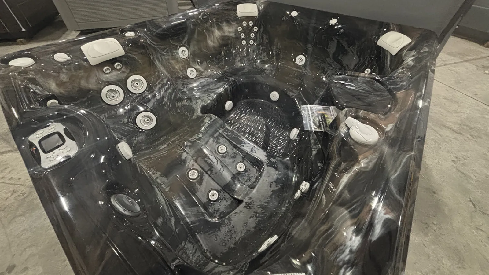 Modern black marble-patterned hot tub with multiple jets and headrests in an indoor showroom.
