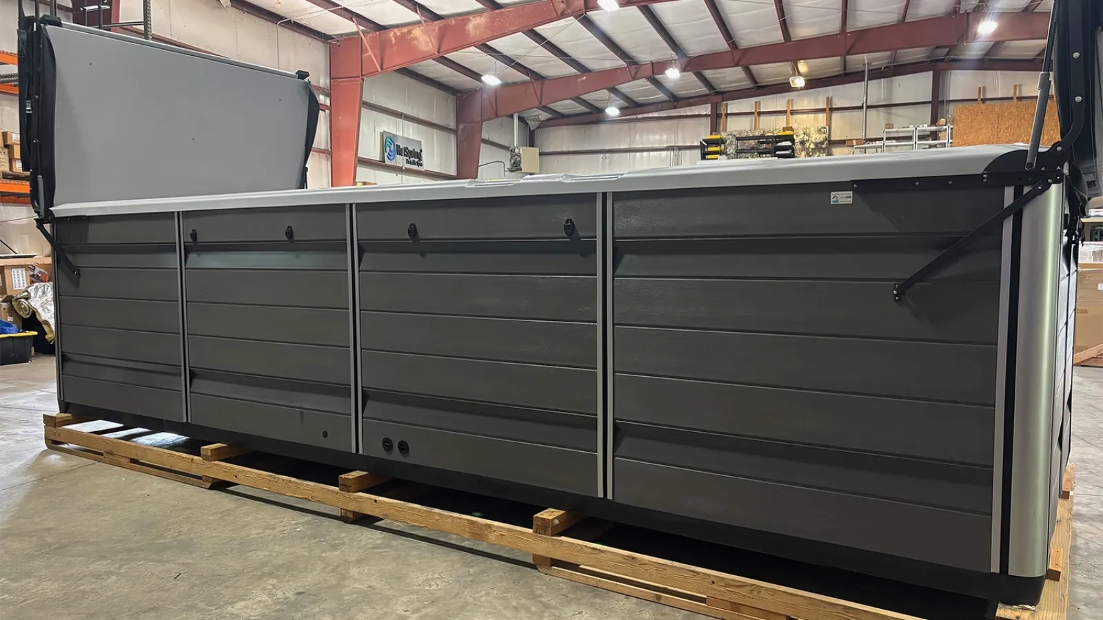 Large dark gray metal container or dumpster on wooden pallets in a warehouse with industrial lighting.
