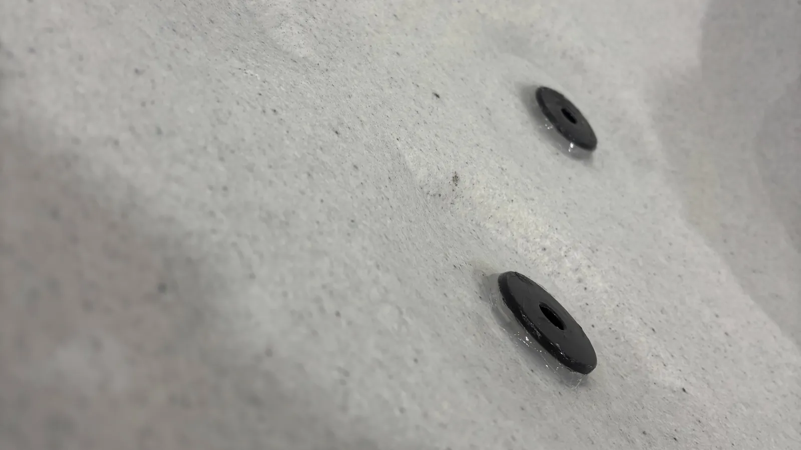 Close-up of a white textured surface with two dark bolts embedded, showing material details and shadows.