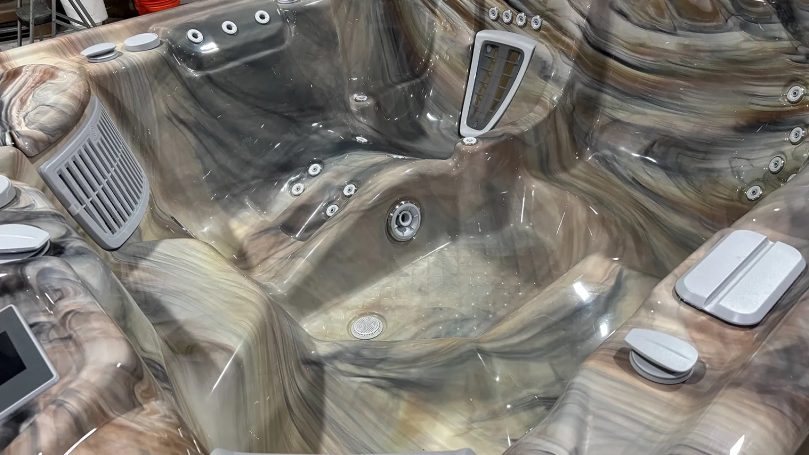 Empty multi-seat luxury hot tub with multiple jets and controls in a glossy marble-like finish.