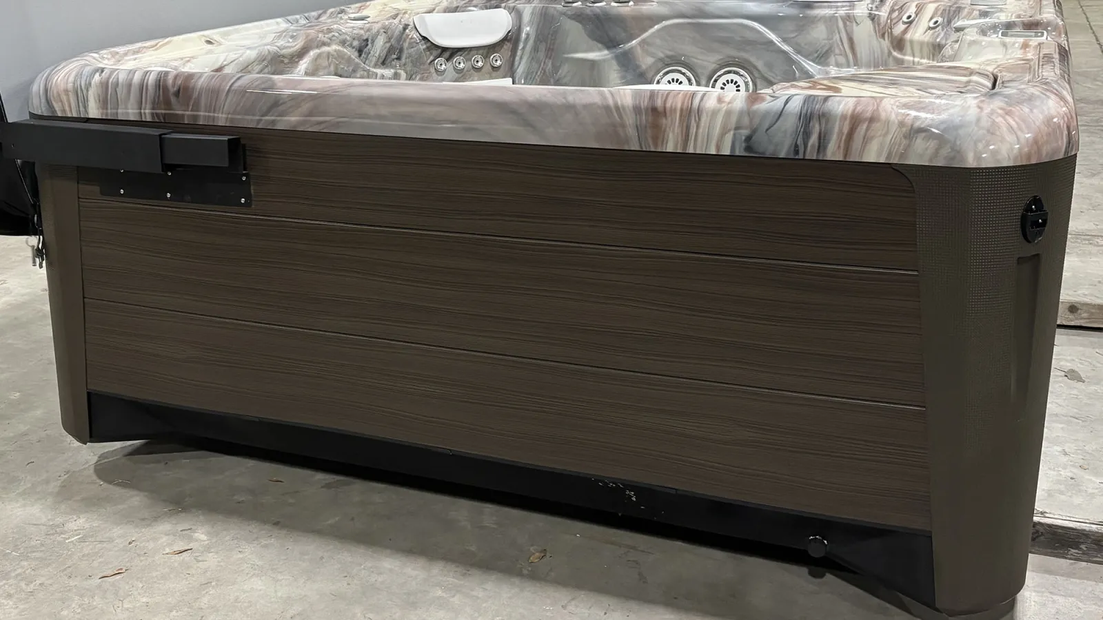 Modern outdoor hot tub with marbled interior and wood-paneled exterior resting on concrete floor indoors