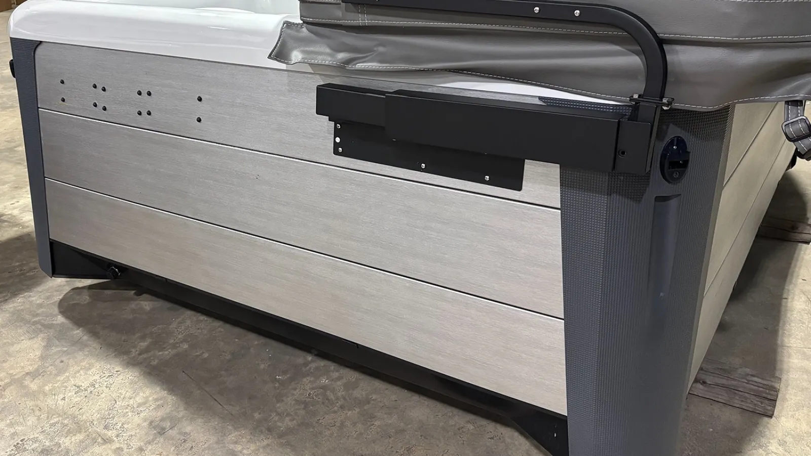 Corner view of a modern outdoor hot tub with gray side panels and a partially covered lid on concrete floor.