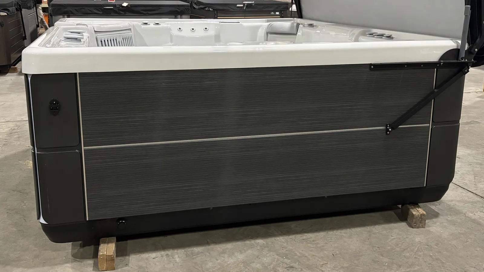 Modern gray and white hot tub with multiple jets and seating on a concrete floor indoors