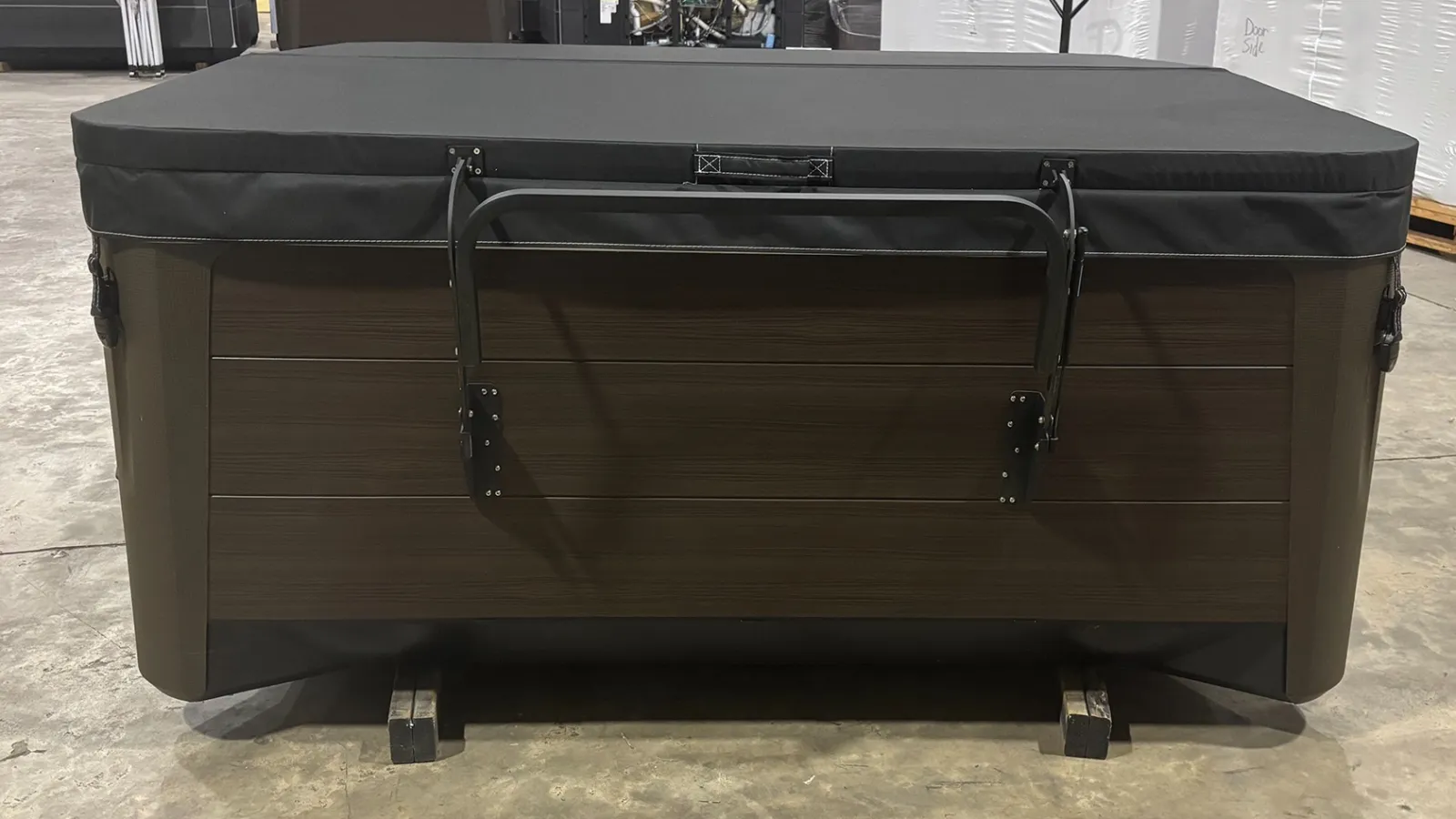 Brown hot tub with black cover and metal handles on a warehouse floor