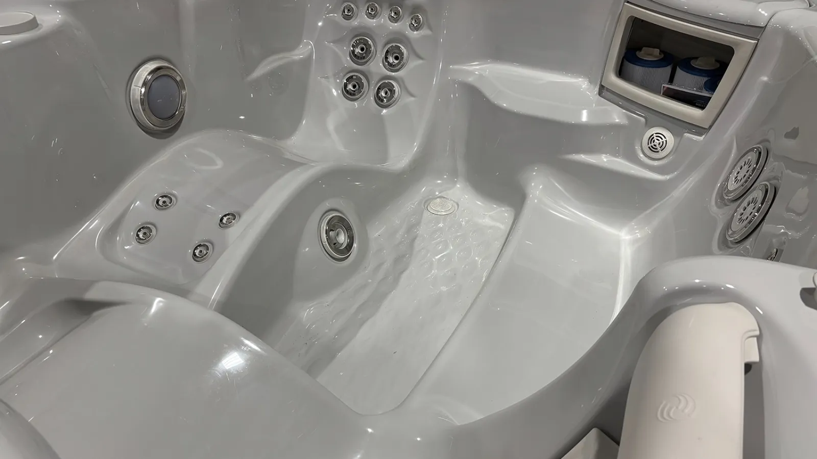 White modern hot tub interior with multiple jets, padded headrests, and built-in storage compartments.