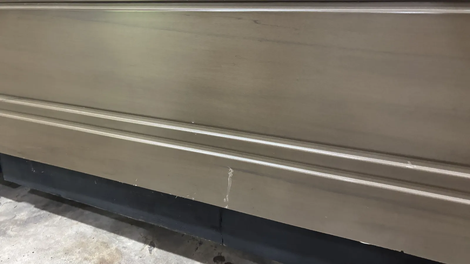 Close-up of a scratched metal surface with horizontal grooves above a black base on concrete floor