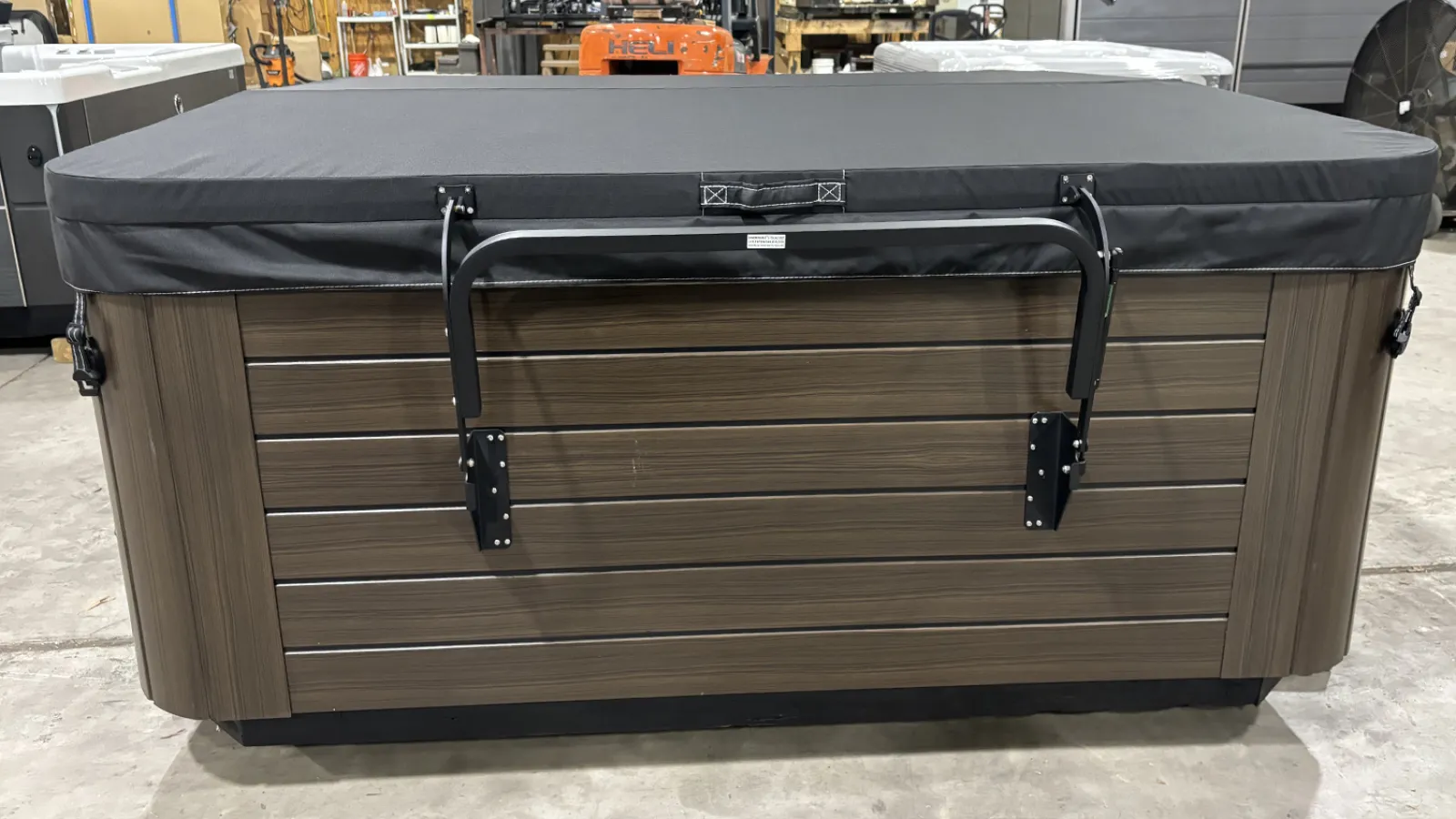 Closed rectangular hot tub with dark wood paneling and black cover in a warehouse setting.
