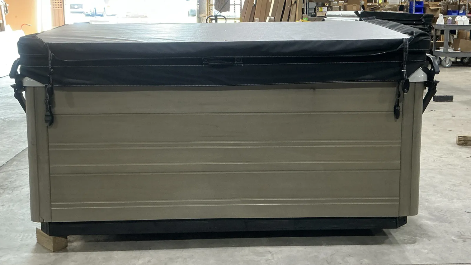 Large rectangular hot tub covered with a tight black cover inside a warehouse setting.