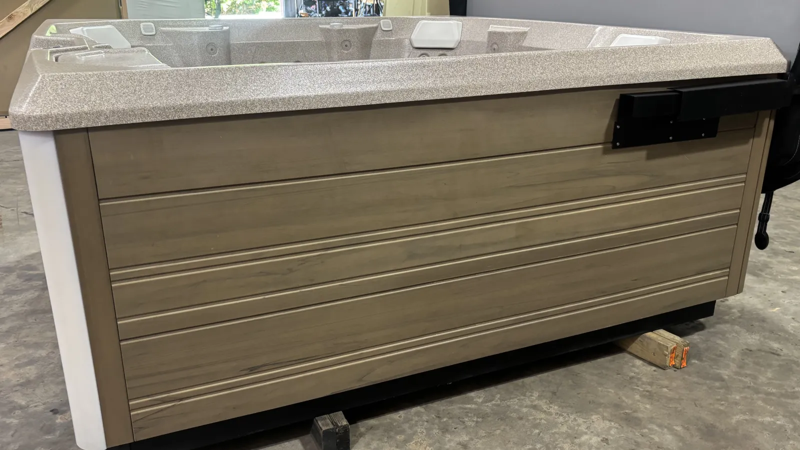 Modern rectangular hot tub with granite top and wood panel exterior on a concrete floor indoors