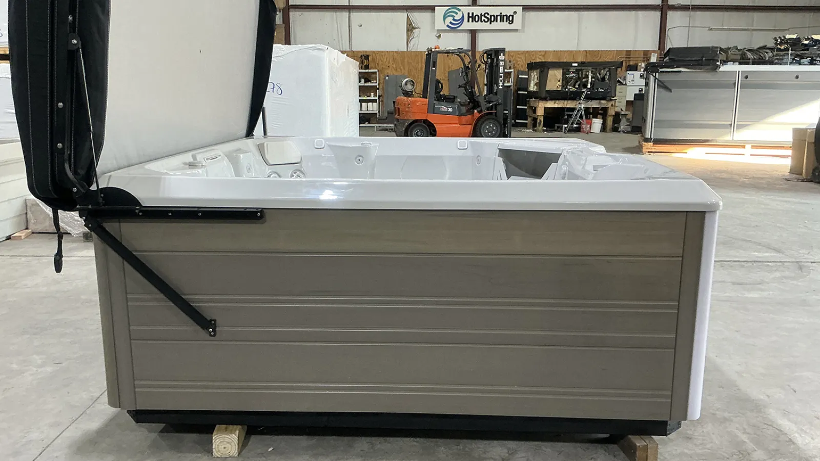 Side view of a beige HotSpring outdoor hot tub with open cover in a warehouse setting.