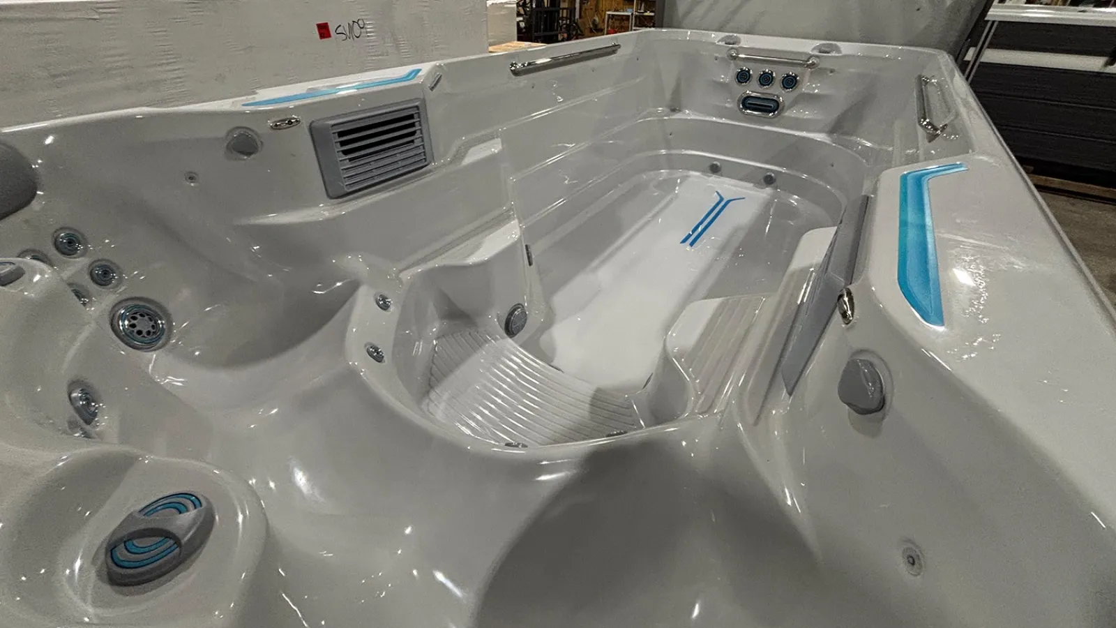 White spacious hot tub with multiple jets and blue accent lighting in an indoor warehouse setting