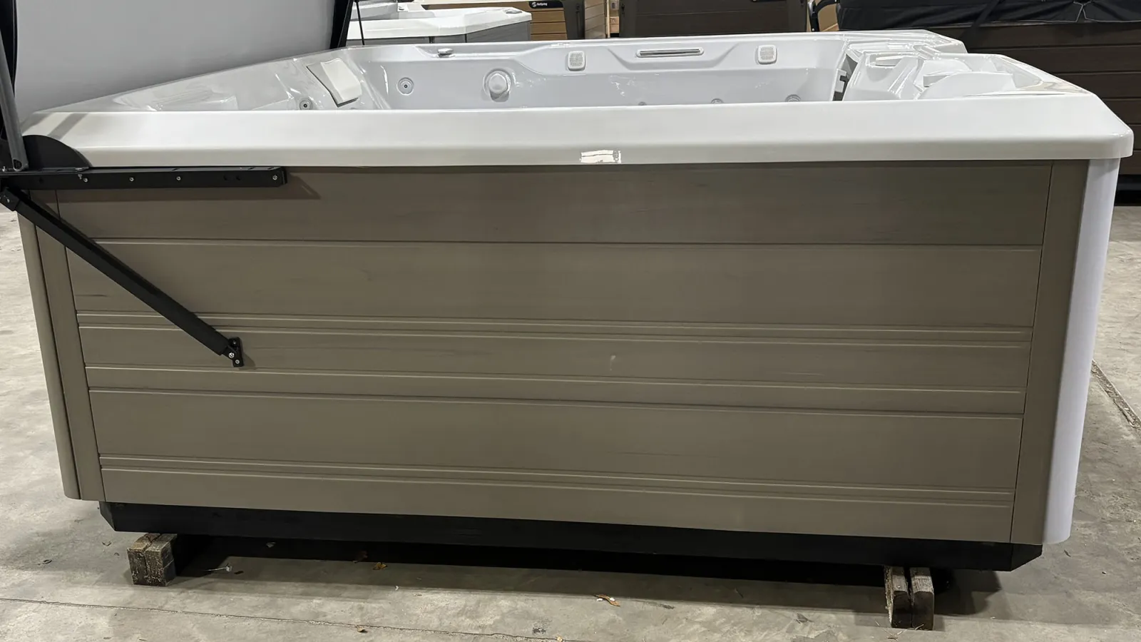 Modern rectangular hot tub with gray wooden paneling and white interior, displayed indoors on concrete floor.