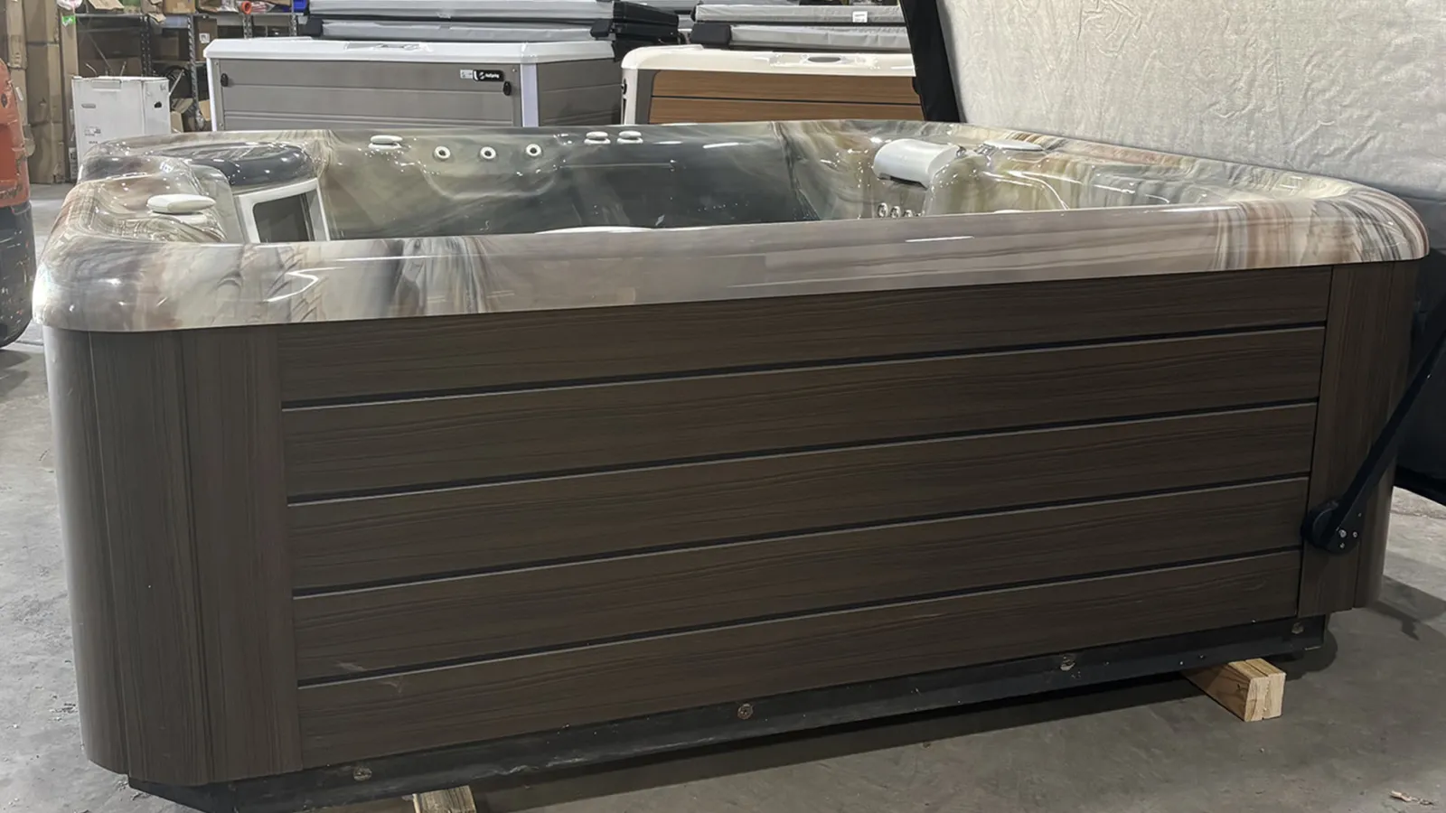 Modern brown and gray hot tub with multiple jets and seating, displayed indoors on wood blocks.