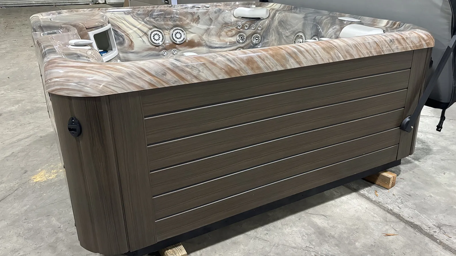 Modern hot tub with marble-patterned interior and wood-paneled exterior on concrete floor indoors.