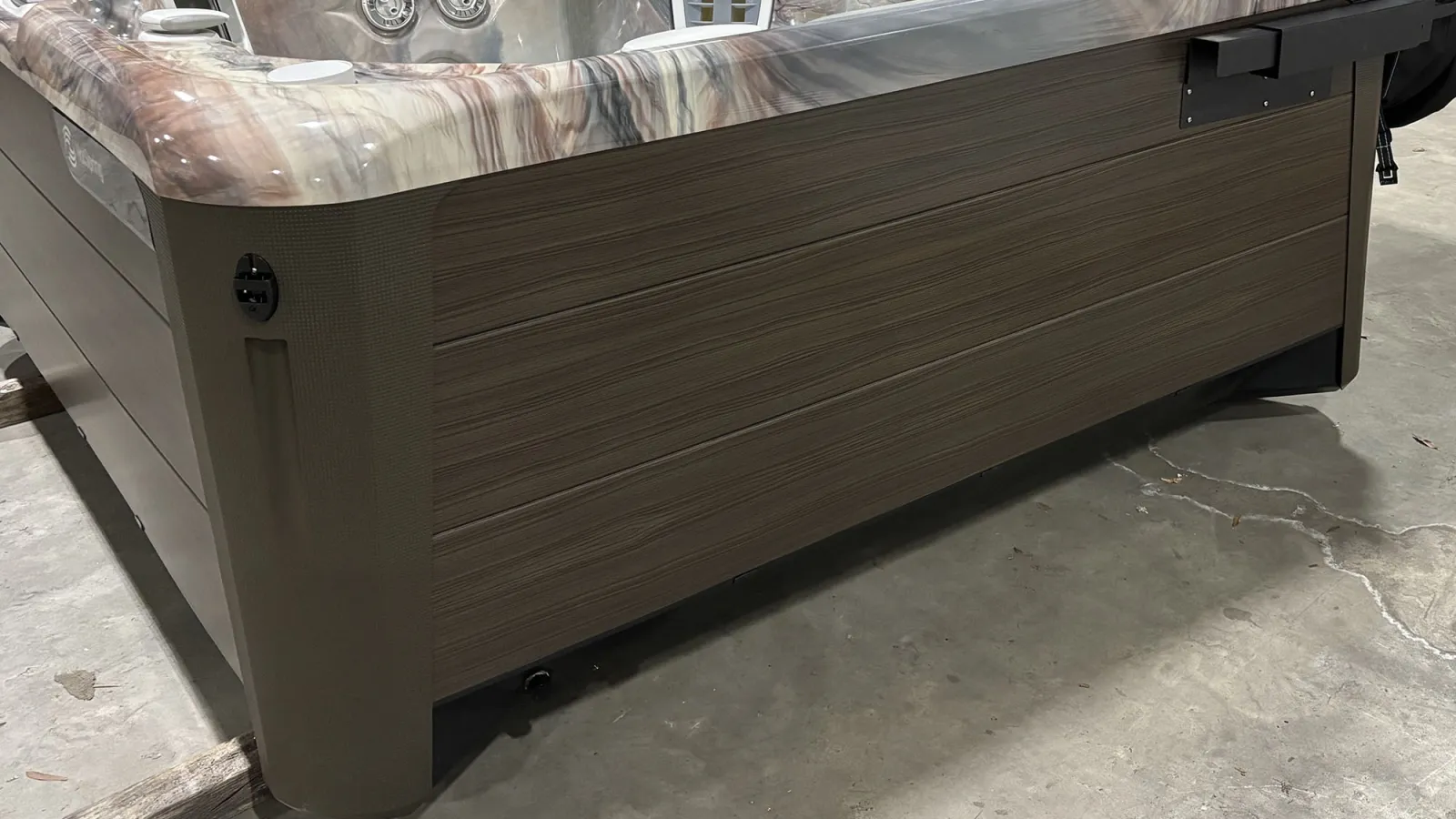 Close-up of a brown spa hot tub exterior with textured panels on a concrete floor indoors.