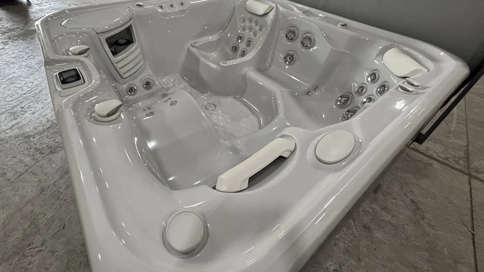 Modern white luxury hot tub with multiple seating areas and built-in jets on a concrete floor.