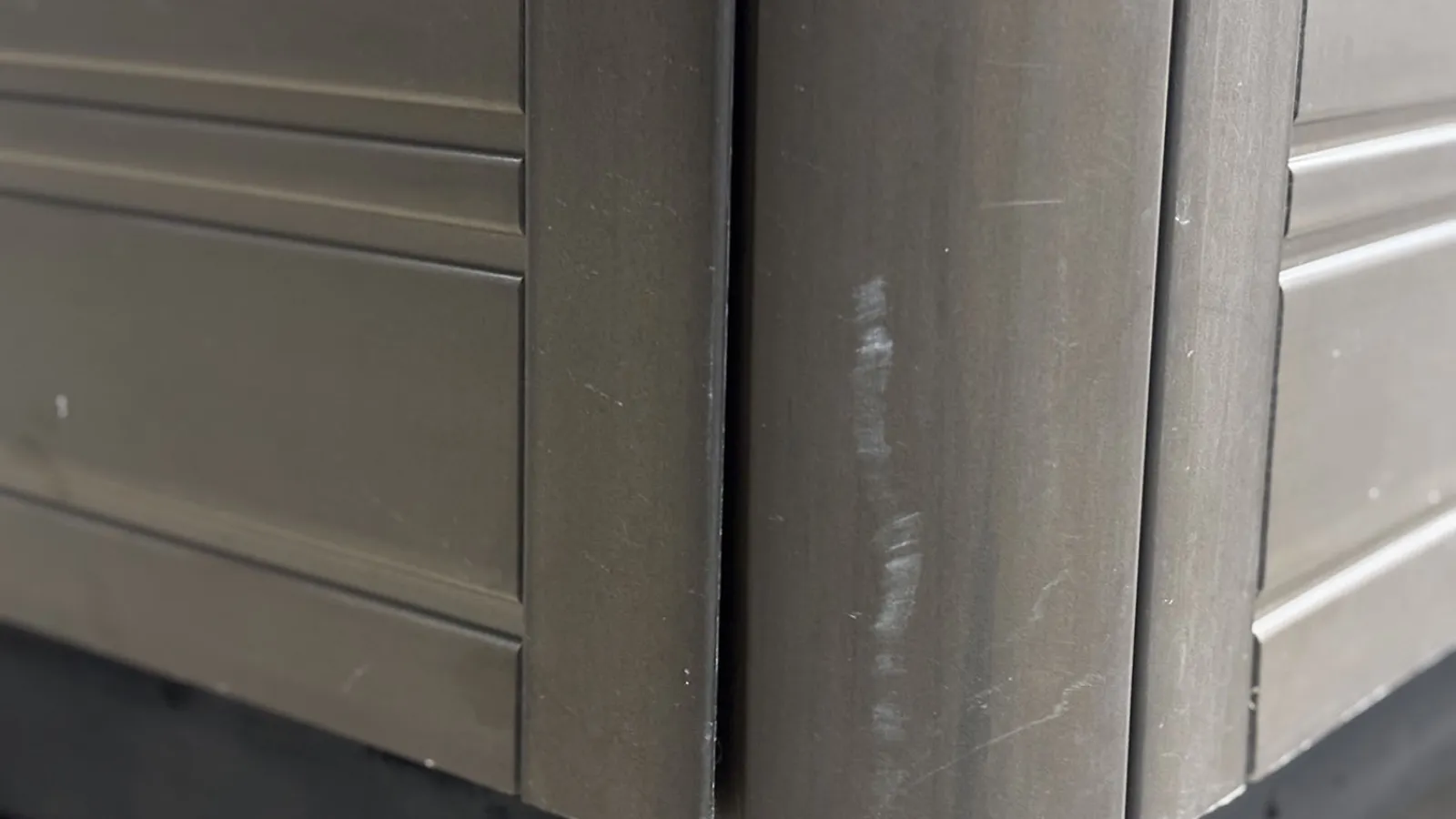 Close-up of a brown scratched corner of a wooden or metal piece of furniture with panel details.