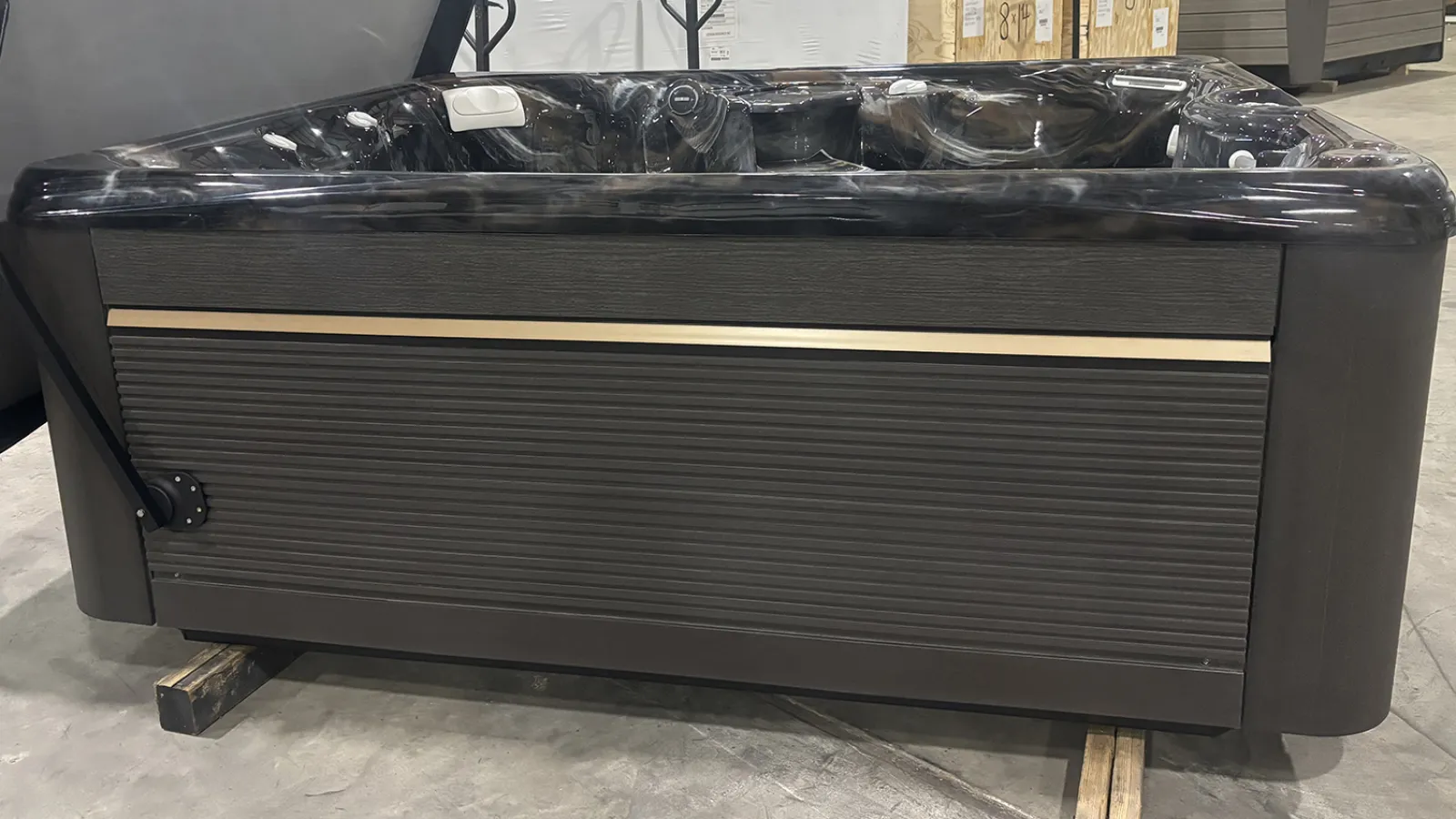 Dark brown outdoor hot tub with textured side panel and beige accent line in warehouse setting.