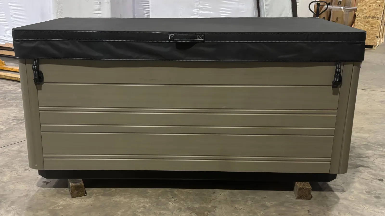 Rectangular storage container with beige sides and a black cover, placed on wooden blocks in a warehouse.