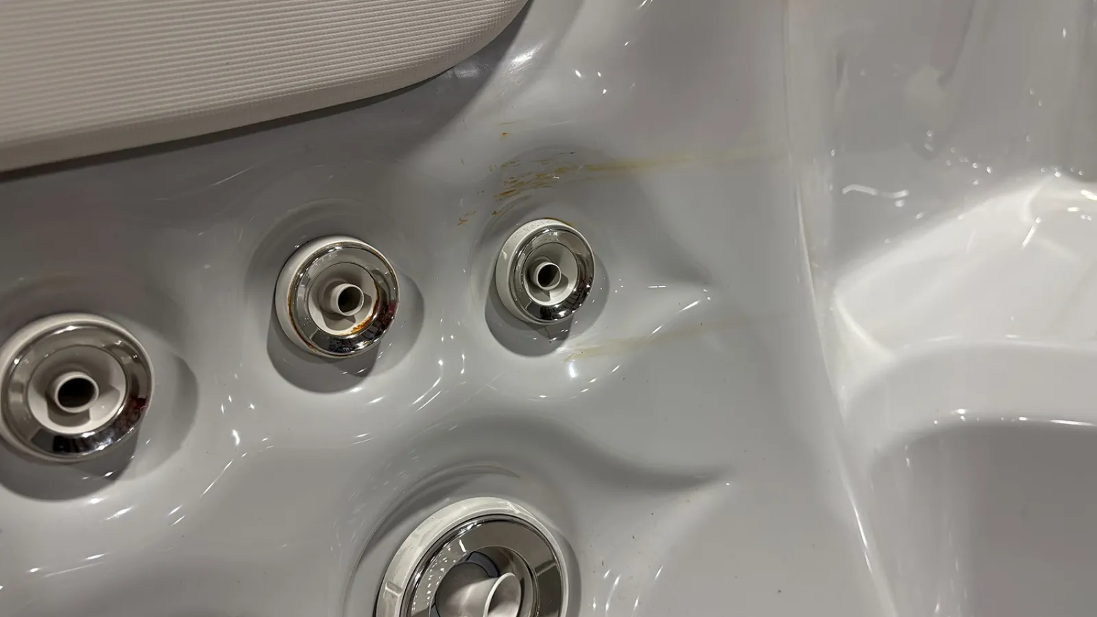 Close-up of jacuzzi spa jets and air nozzles on a clean white hot tub surface with slight scuff marks.