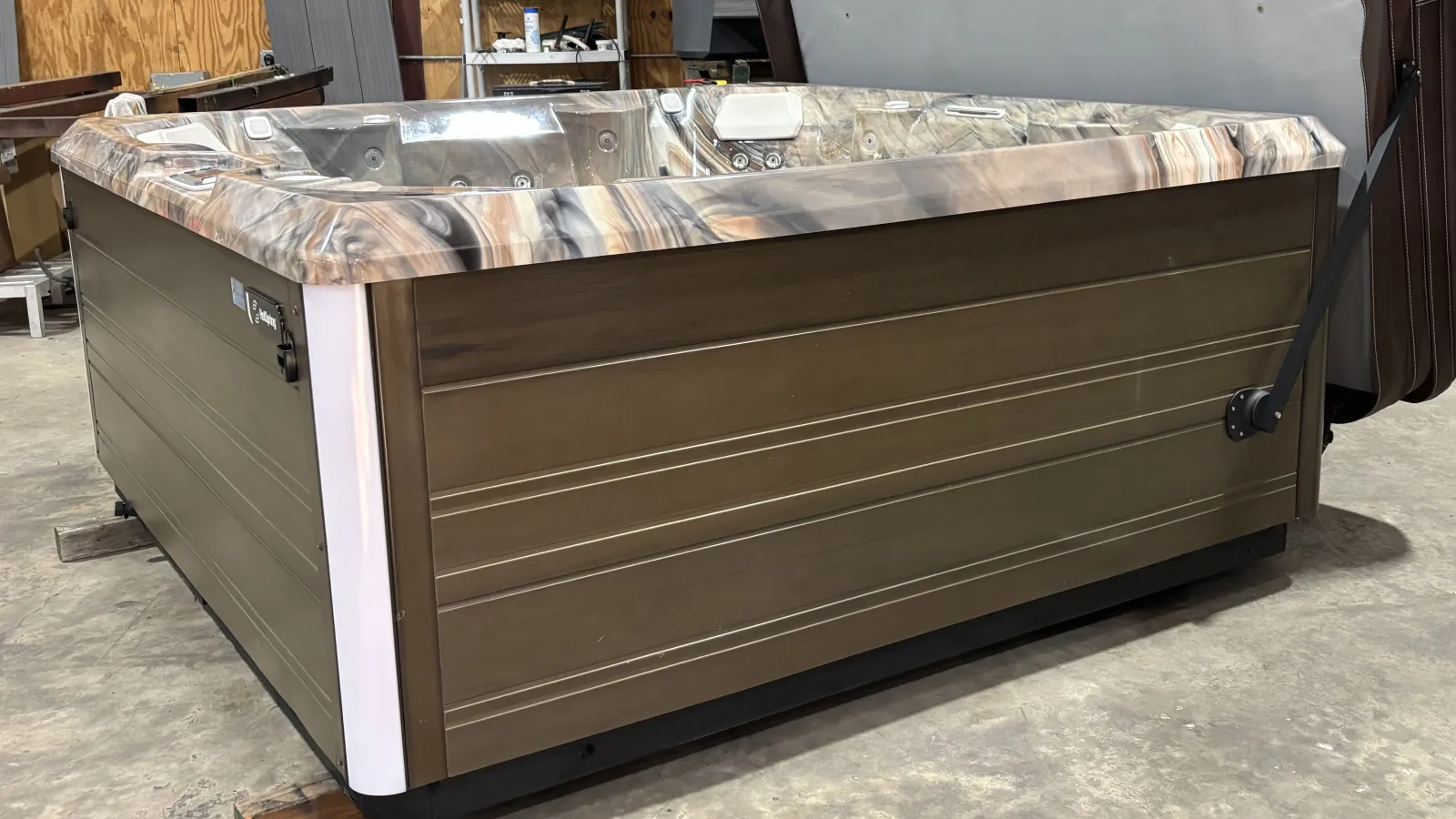 Large rectangular outdoor hot tub with brown paneling and marbled interior in warehouse.
