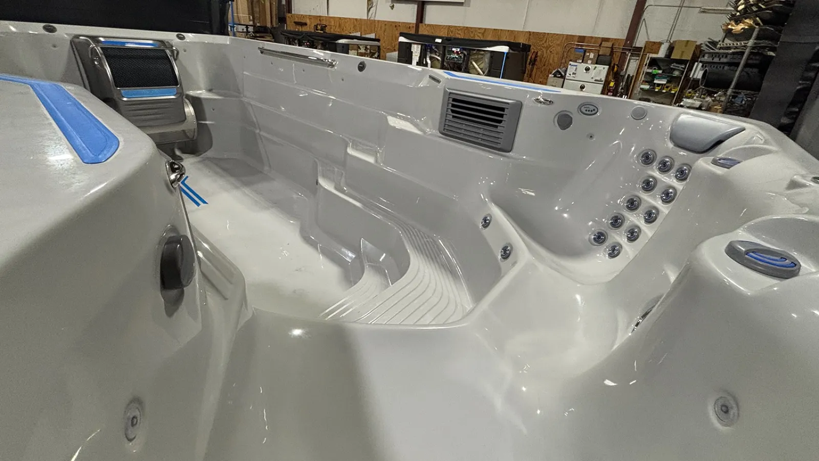 Empty modern white hot tub with multiple seats, jets, and controls inside a showroom setting.
