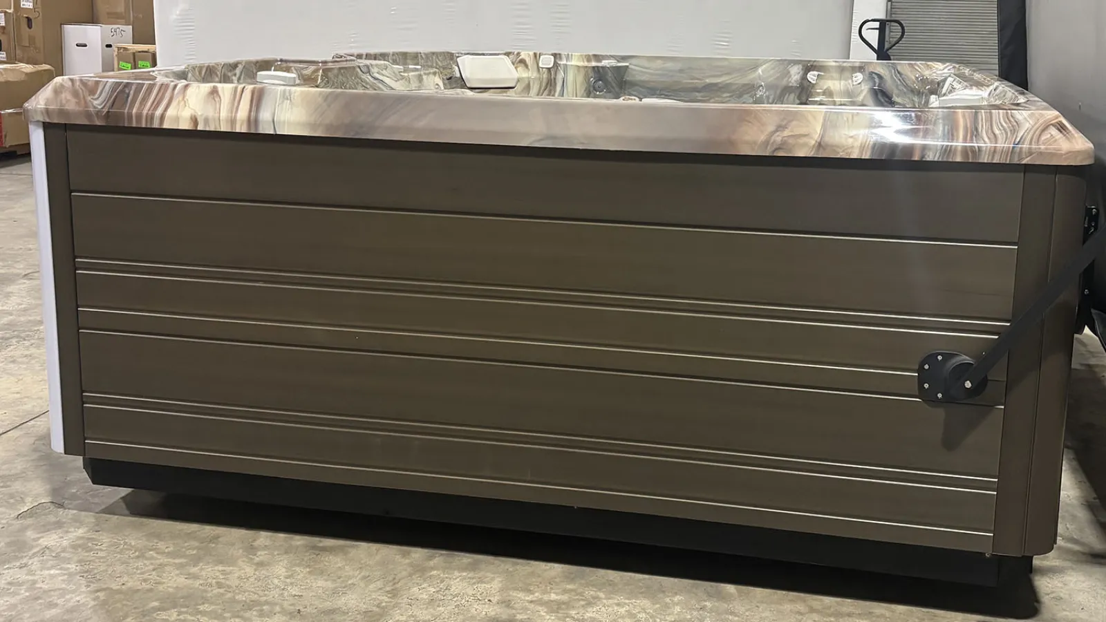 Rectangular brown hot tub with marble-like edge resting on concrete floor in warehouse