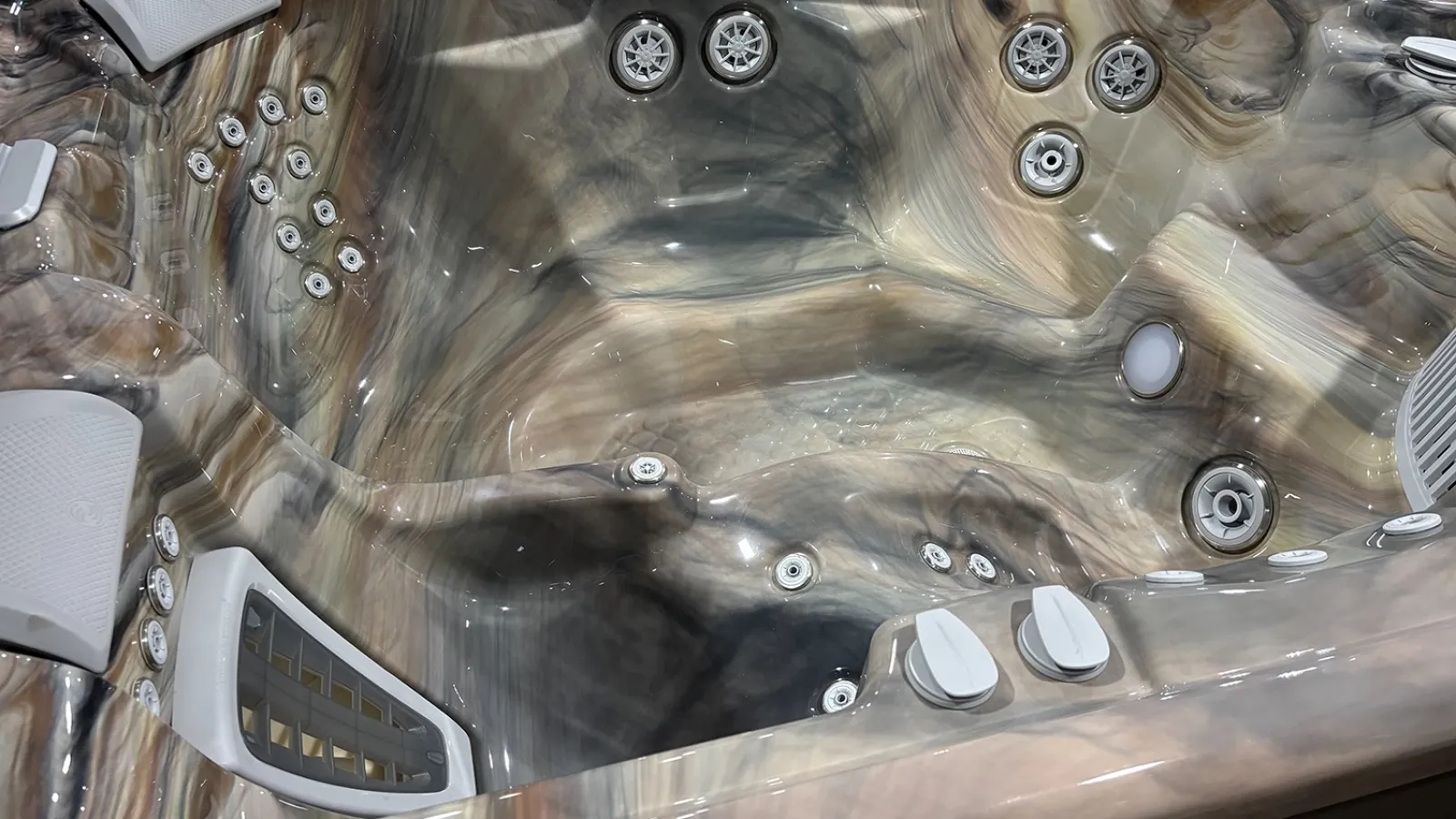 Empty luxury hot tub with multiple jets and silver-brown marbled interior surface under bright lighting