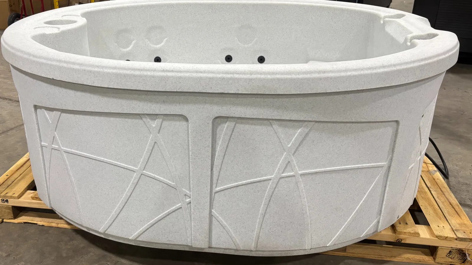 White round hot tub with textured exterior and built-in cup holders on wooden pallet indoors.