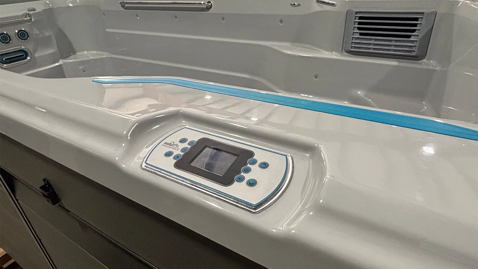 Control panel and seating area of a modern white swim spa with blue trim and built-in jets.