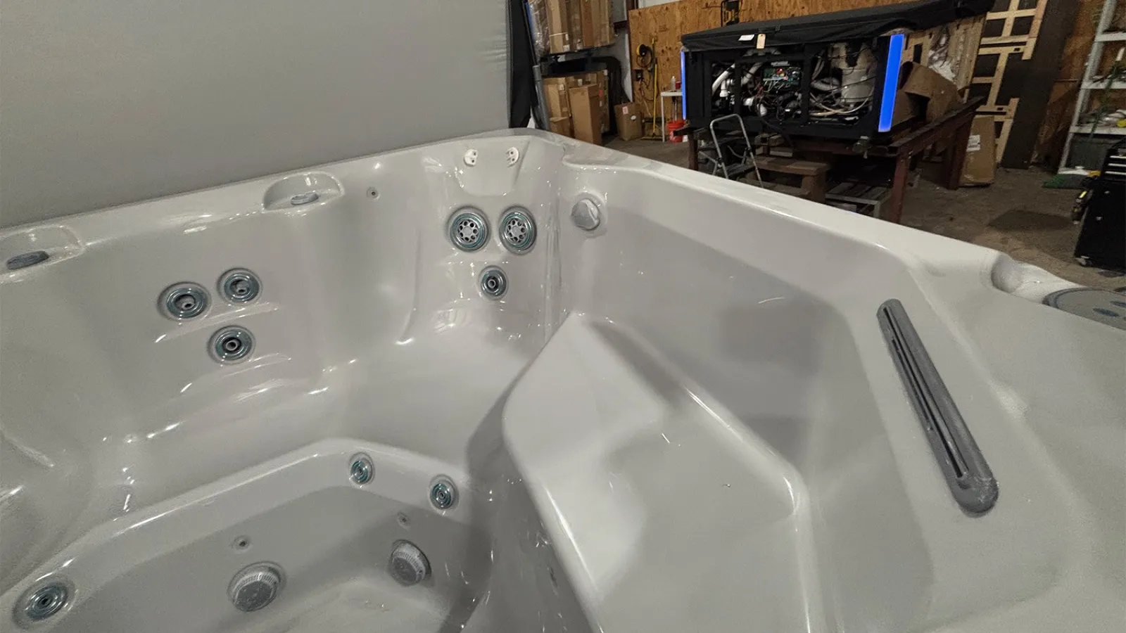Empty white hot tub with multiple water jets in an indoor warehouse setting with equipment in the background
