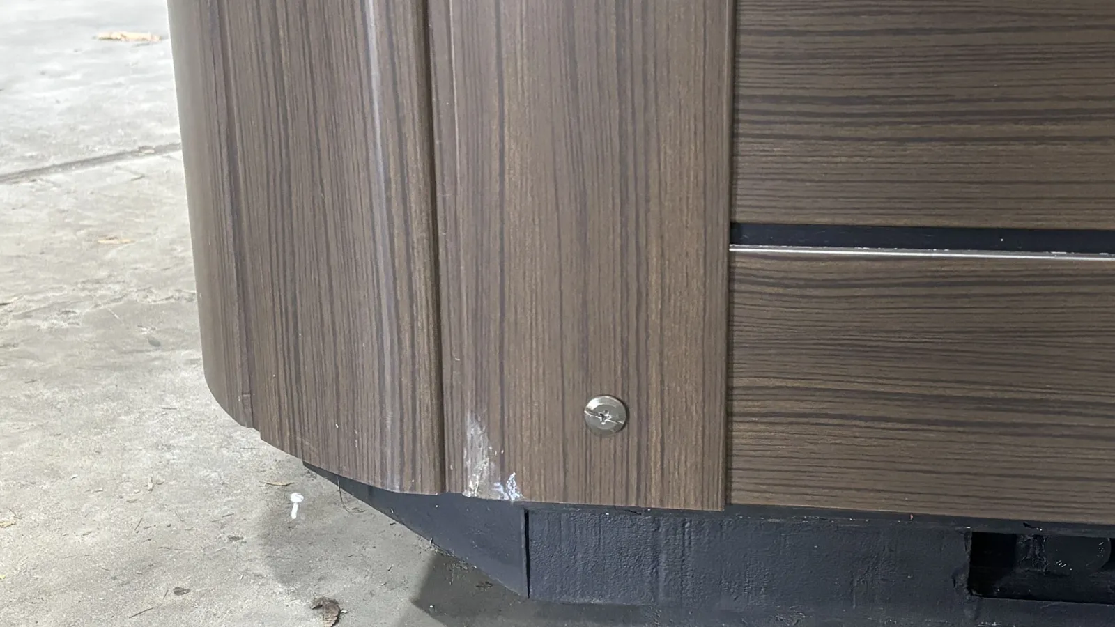 Close-up of curved wood panel with screw on black base on concrete floor with paint marks.
