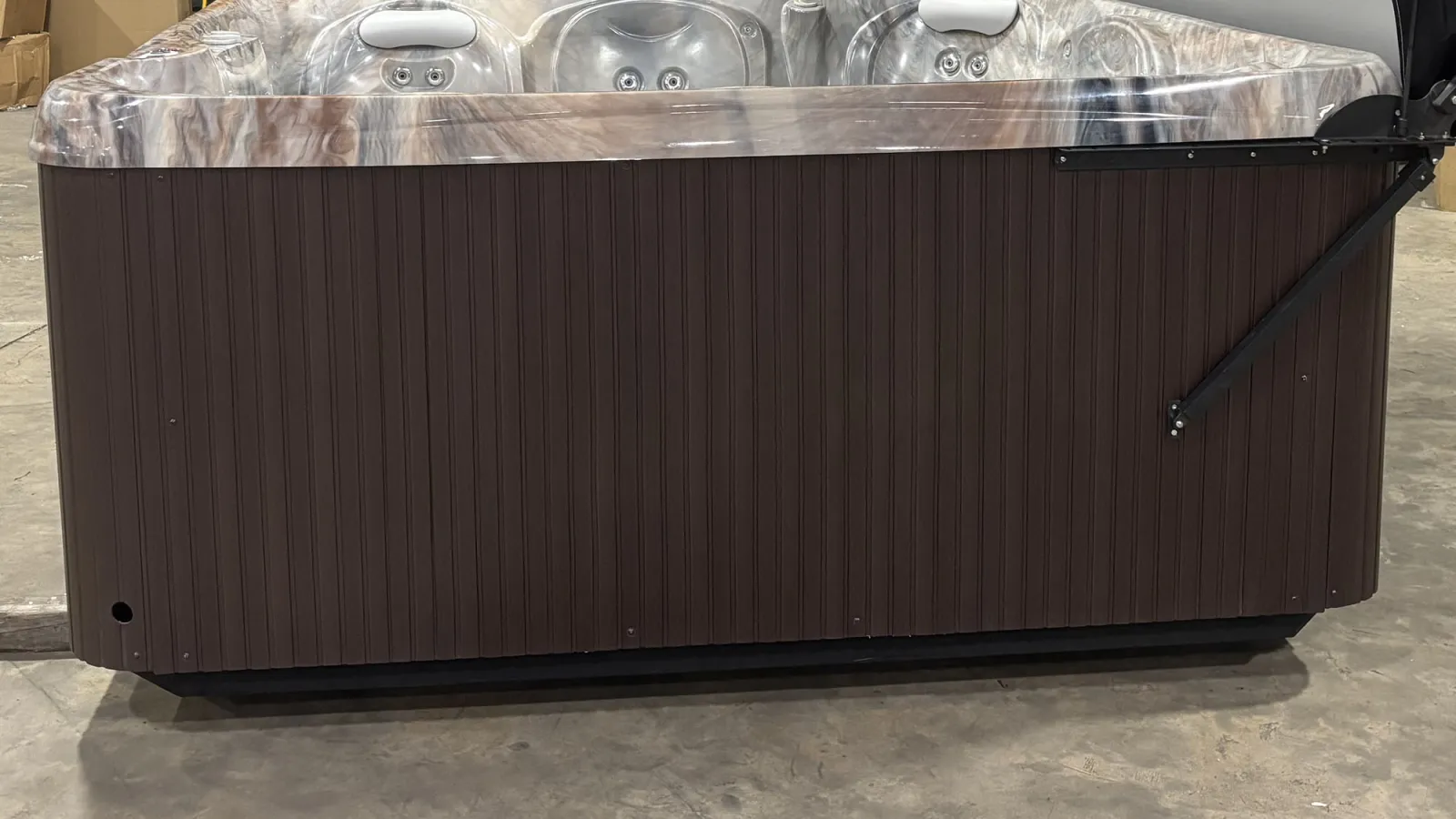 Modern outdoor hot tub with compact brown wooden exterior and silver interior jets on concrete floor.